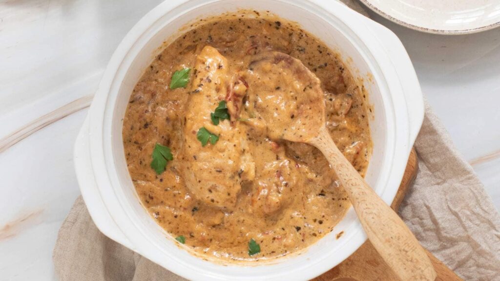 Marry me chicken in a white pot with a wooden spoon.