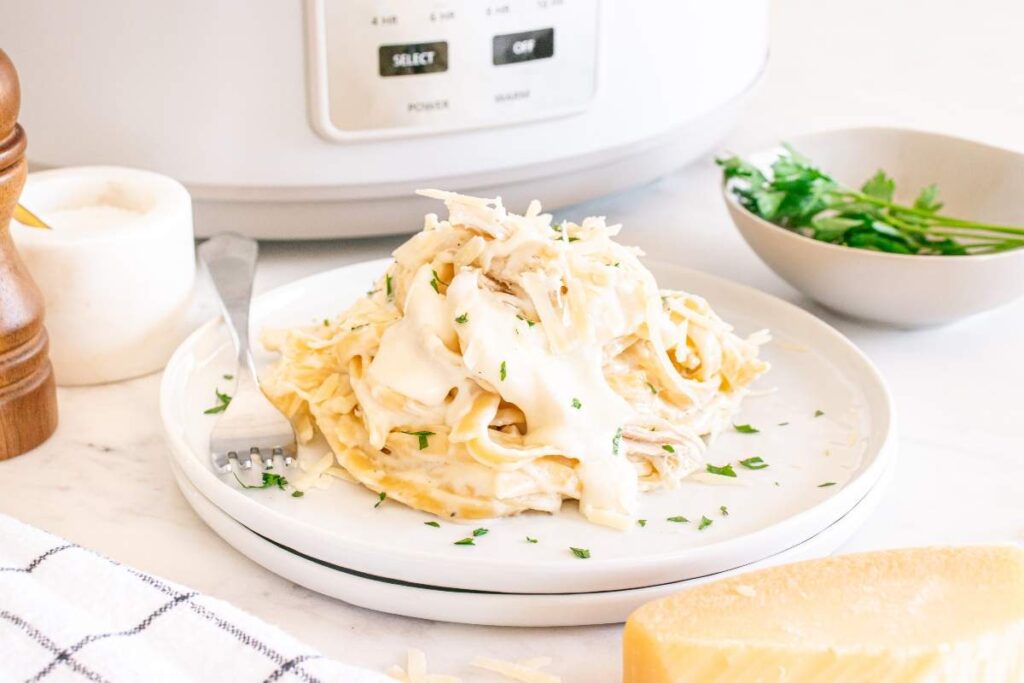 A plate of creamy slow cooker chicken fettuccine Alfredo topped with shredded chicken and garnished with parsley.
