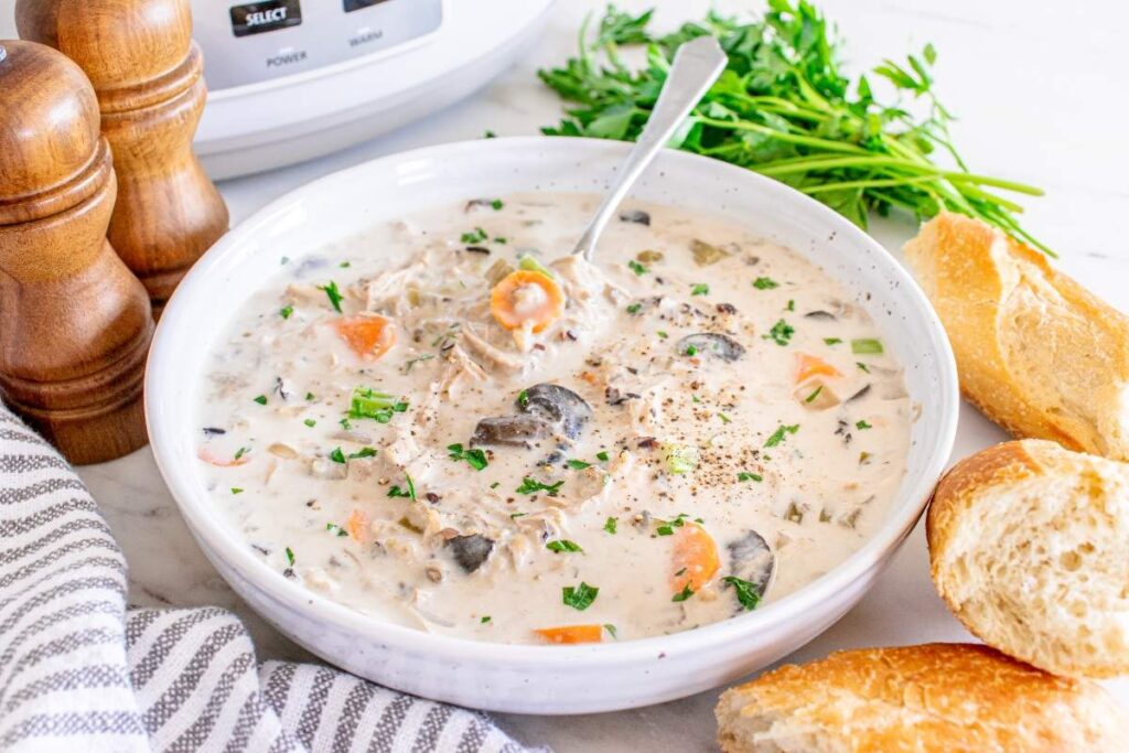 A bowl of creamy Slow Cooker Chicken Wild Rice Soup garnished with parsley, served with a spoon inside.