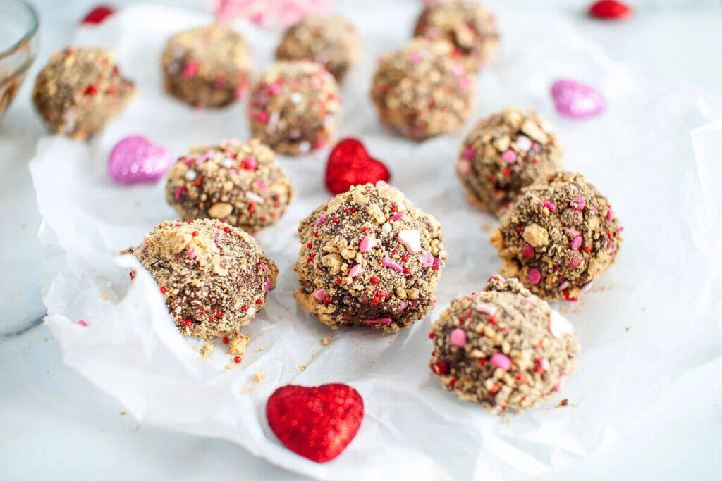 S’more truffles coated in crushed sprinkles and decorated with red and pink hearts, made easily with a boxed brownie mix for Valentine’s Day.