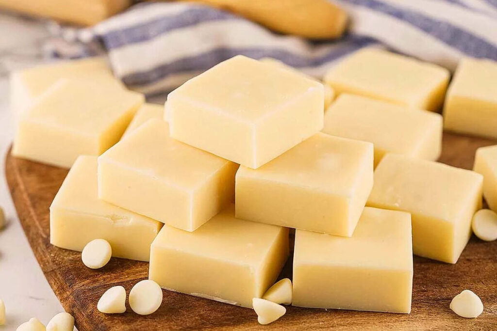 Vanilla fudge blocks sit on a wooden board with white chocolate chips scattered around.