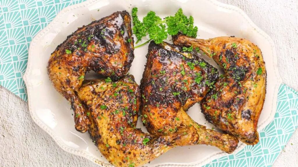 A white platter with four seasoned and cooked chicken quarters, garnished with fresh parsley.