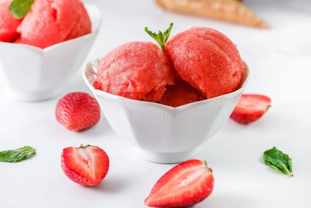 White bowl with scoops of strawberry sorbet, made with frozen strawberries and just 4 ingredients, garnished with mint.