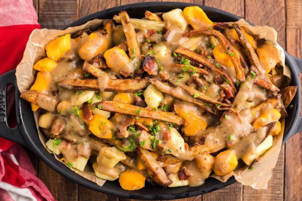 Canadian poutine with fries, cheese curds, hearty gravy, and bacon served in a black dish on a wooden table.