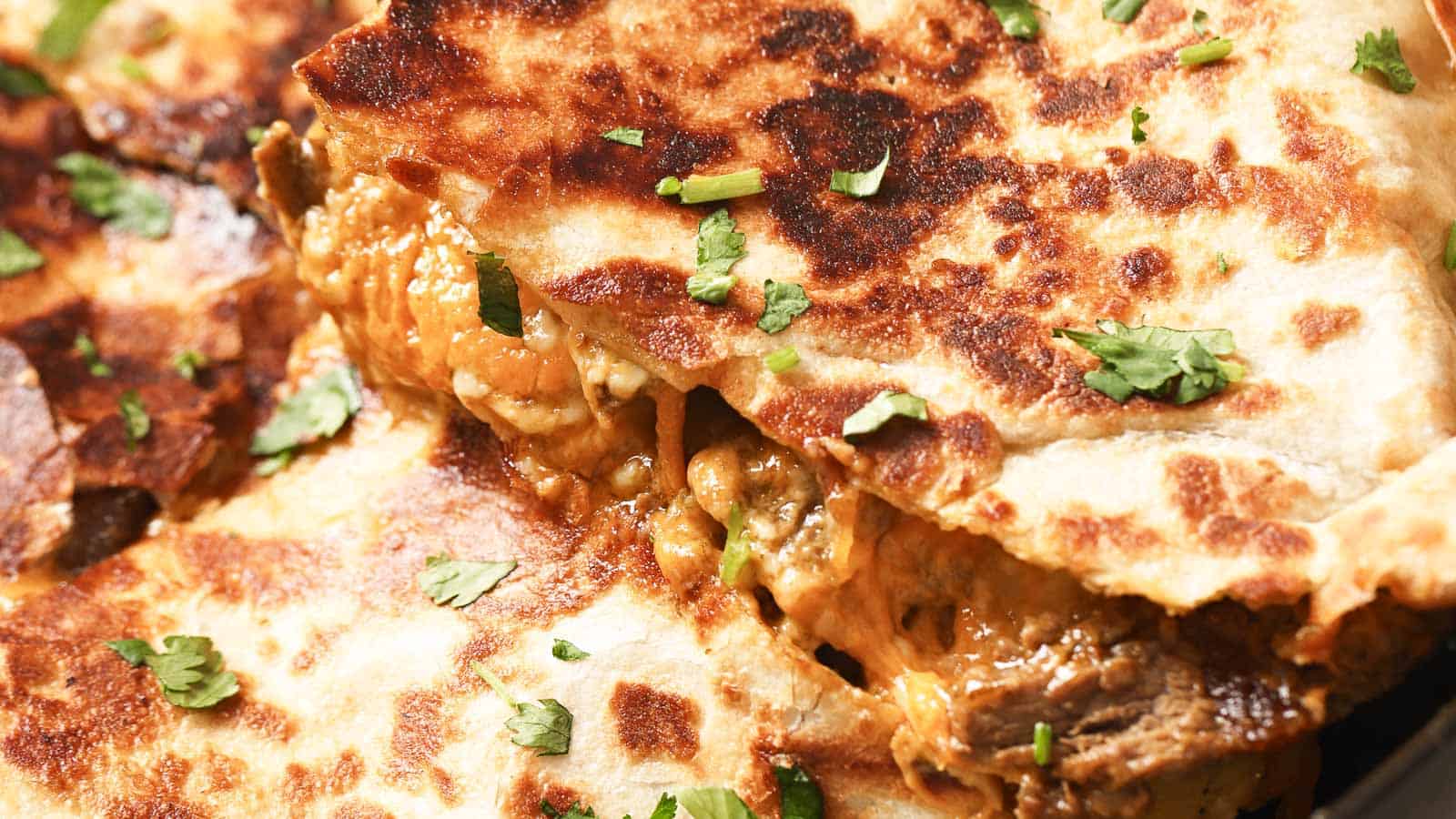 A closeup shot of a carne asada quesadilla topped with cilantro and sour cream.