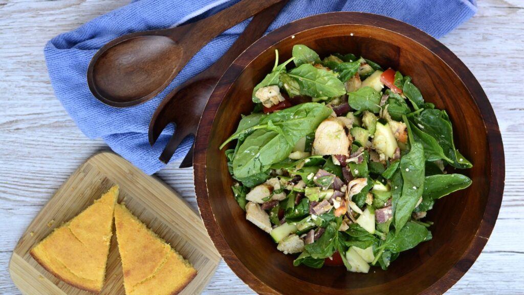 An overhead shot of a wooden serving bowl filled with salad next to cornbread on a cutting board.