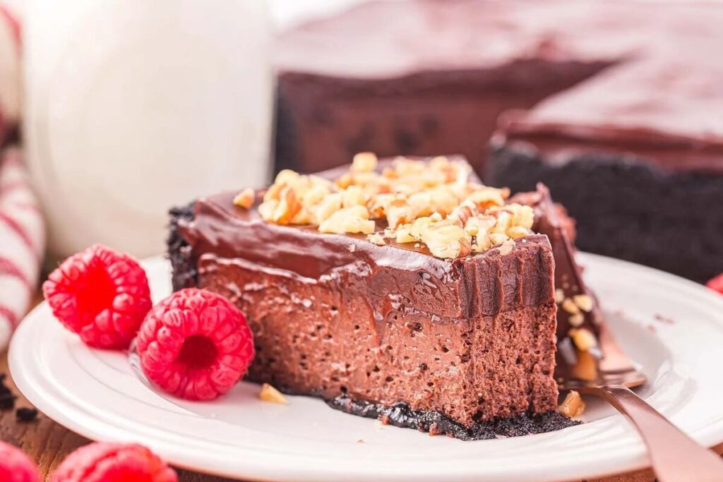 A decadent slice of chocolate cheesecake adorned with crunchy walnuts sits elegantly on a white plate, accompanied by vibrant raspberries.