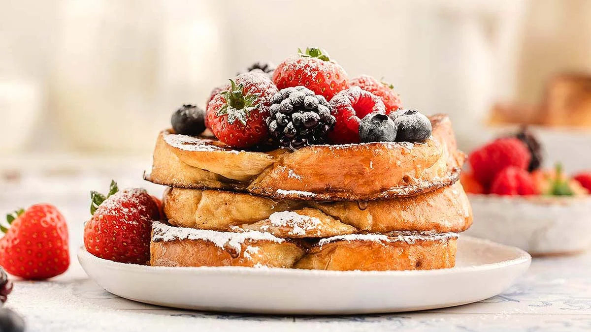 Three slices of French toast topped with powdered sugar, strawberries, blackberries, and blueberries.
