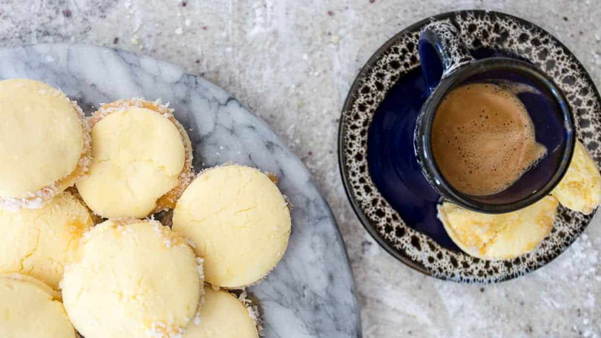 Alfajores cookies filled with dulce de leche and rolled in grated coconut, on a marble plate.