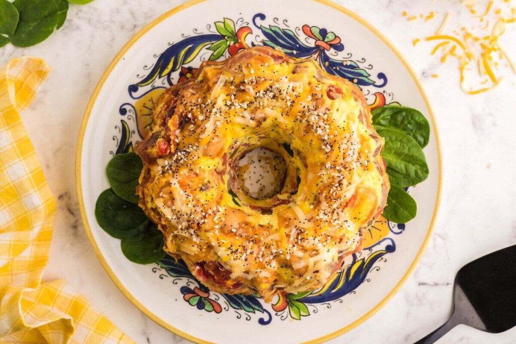 A savory ring cake adorned with seeds and cheese sits elegantly on a decorative plate, garnished with fresh spinach leaves.