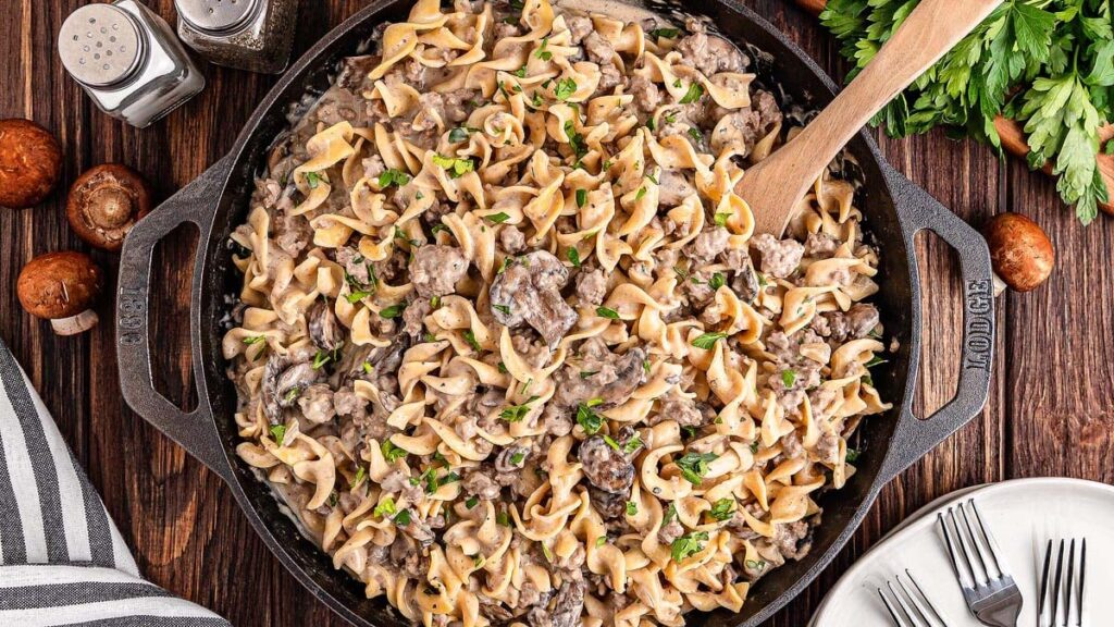 A plate of ground beef stroganoff with noodles and mushrooms, topped with chopped herbs.