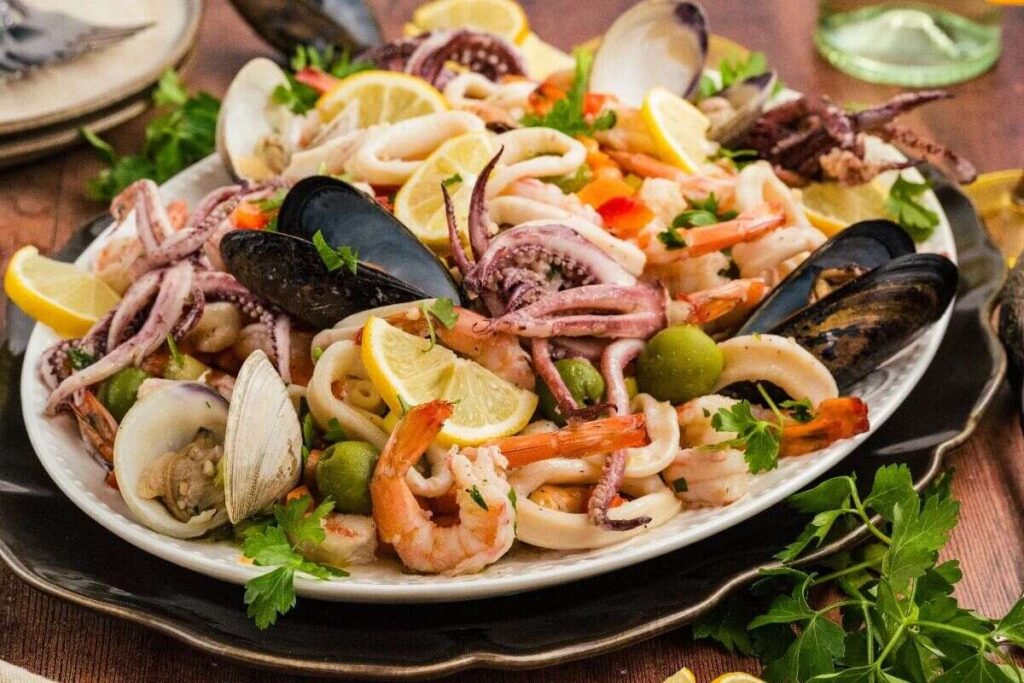 A platter of Italian Seafood Salad featuring shrimp, mussels, clams, squid, olives, and lemon wedges.