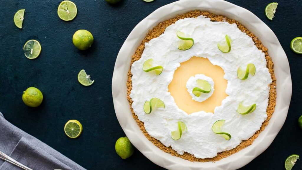 Key lime pie with a graham cracker crust, topped with coconut whipped cream and garnished with lime slices.