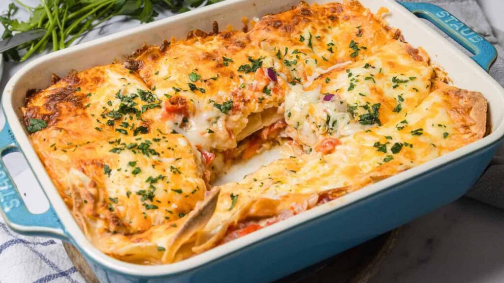 A cheesy baked casserole in a blue dish, with a square piece removed and herbs sprinkled on top.