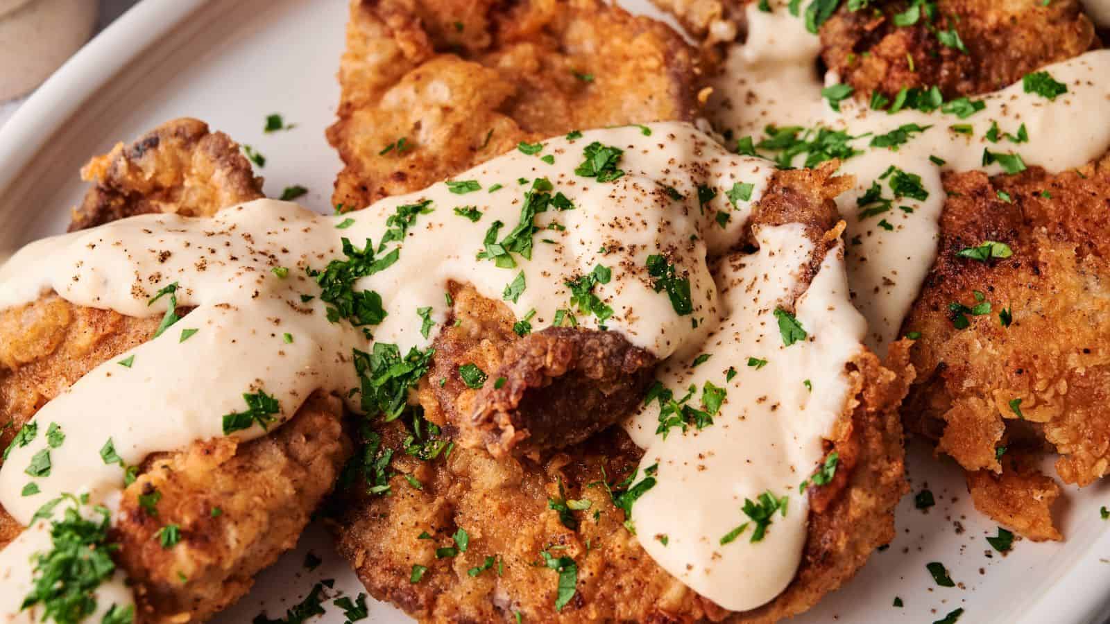 Breaded and fried steak pieces topped with creamy white gravy and chopped parsley on a white plate.