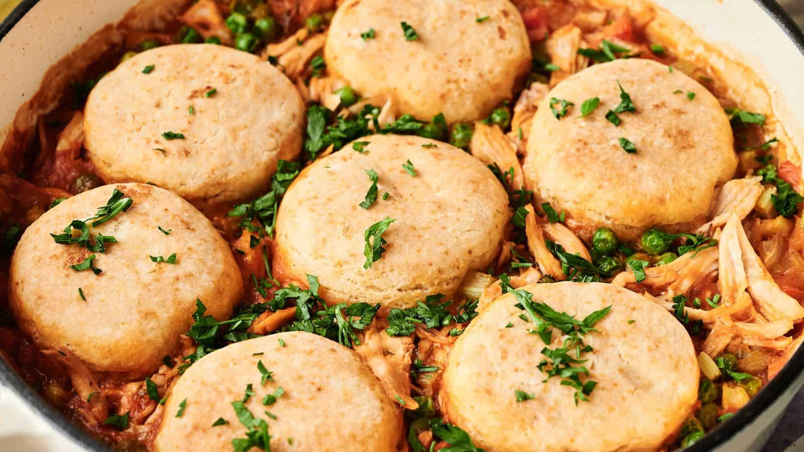 A close-up of a baked chicken pot pie topped with six round biscuits and garnished with chopped parsley.