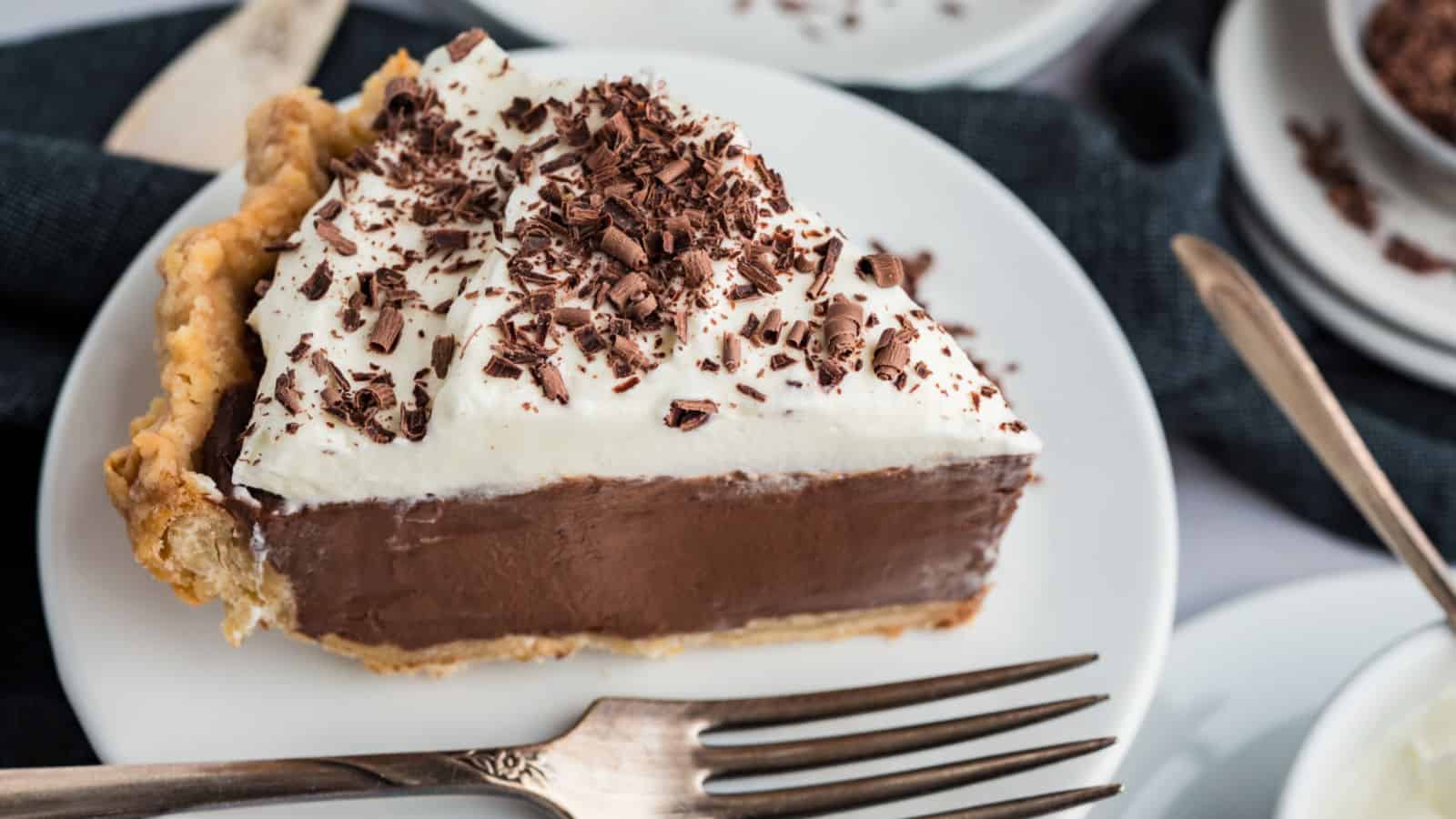 Slice of chocolate cream pie on white plate with fork.