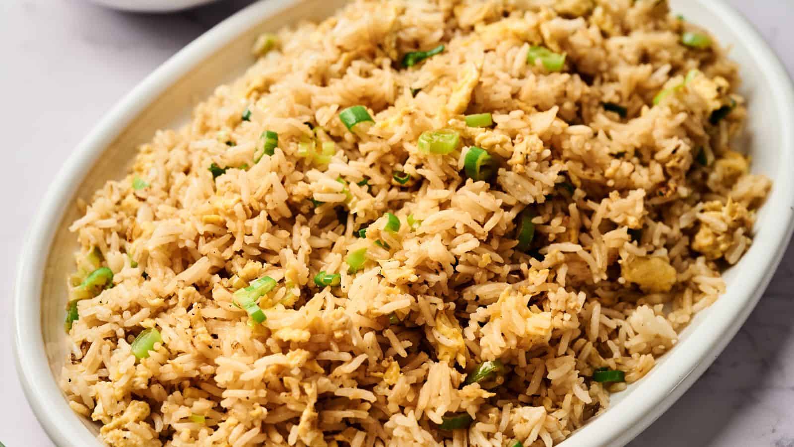 A bowl of Egg Fried Rice with green onions, and diced vegetables, served in a speckled ceramic bowl.