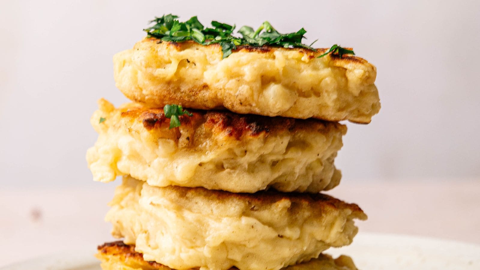 Three golden-brown fritters stacked on a plate, garnished with chopped green herbs on top.