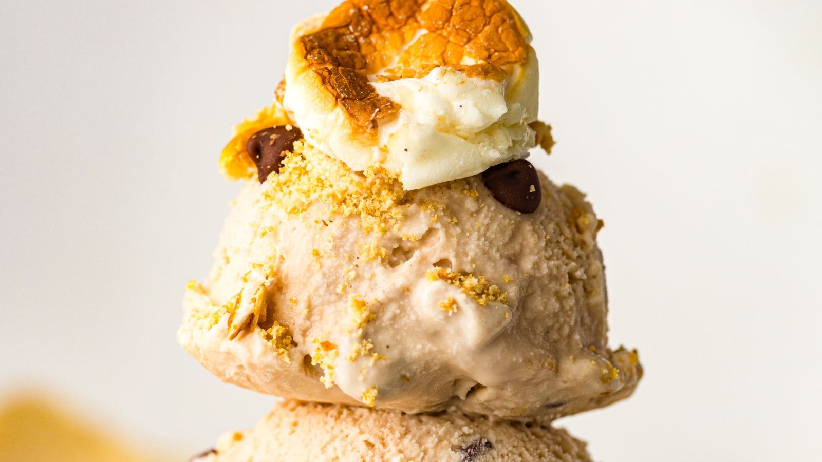 Two scoops of ice cream topped with a toasted marshmallow, chocolate chips, and crumbled cookie bits.
