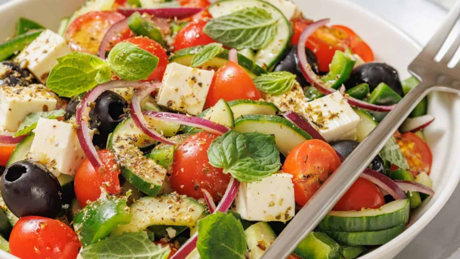 A spoon drizzles dressing over a bowl of Farmhouse Veggie Salad with Feta.