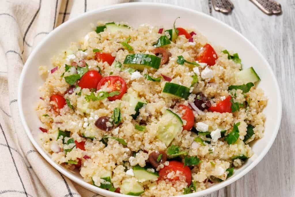 A white bowl of Mediterranean Quinoa Salad on a light blue tablecloth.