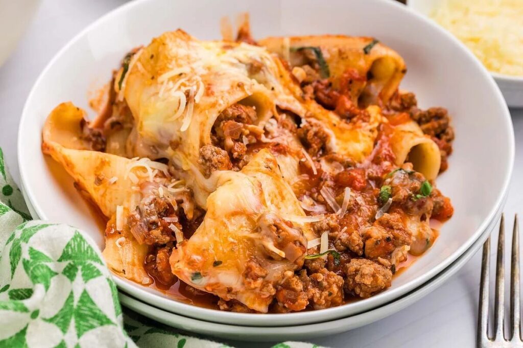 A plate of baked paccheri pasta with meat, tomato sauce, and melted cheese, garnished with herbs.