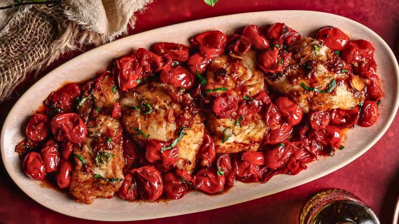 Pan-seared cod fillet topped with blistered cherry tomatoes and herbs on a clean white plate.