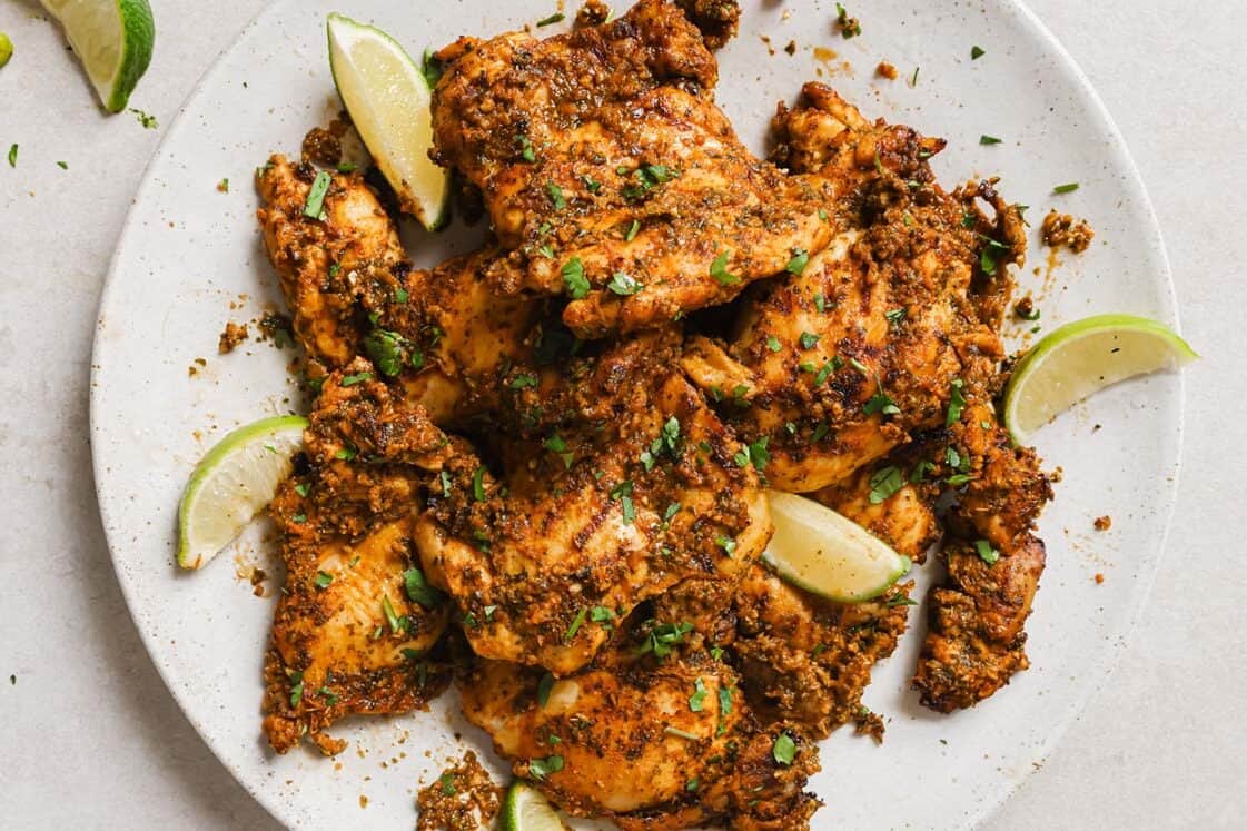 Pollo asado on a white plate with lime wedges.