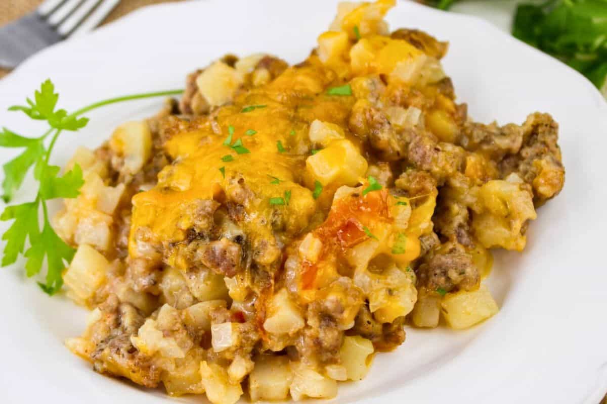 A white plate with a casserole dish, including ground meat, potatoes, and melted cheese, garnished with a parsley sprig.