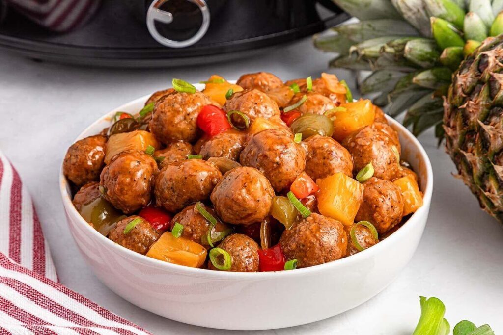 Bowl of Slow Cooker Sweet and Sour Meatballs mixed with pineapple chunks, red and green bell peppers, and sliced green onions.