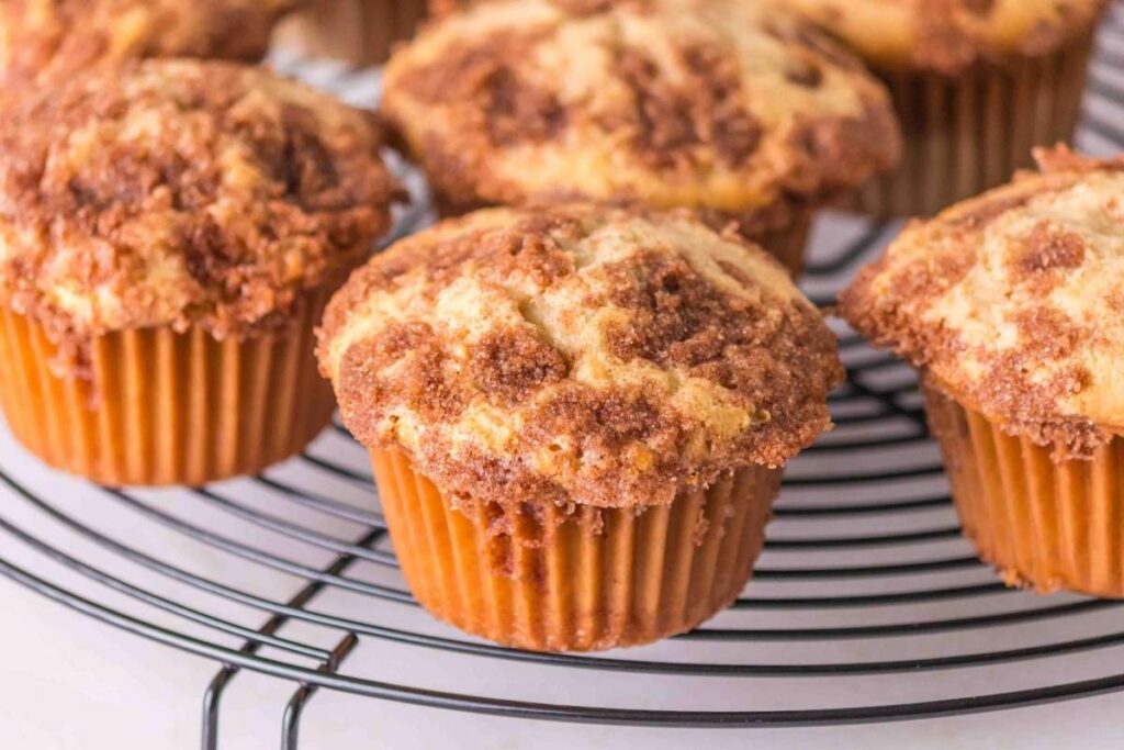 Close-up of freshly baked snickerdoodle muffins with a crumbly topping on a cooling rack.