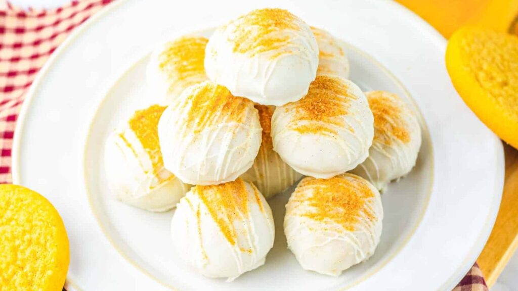 A plate of white chocolate-coated dessert balls topped with golden cookie crumbs, stacked in a pyramid.