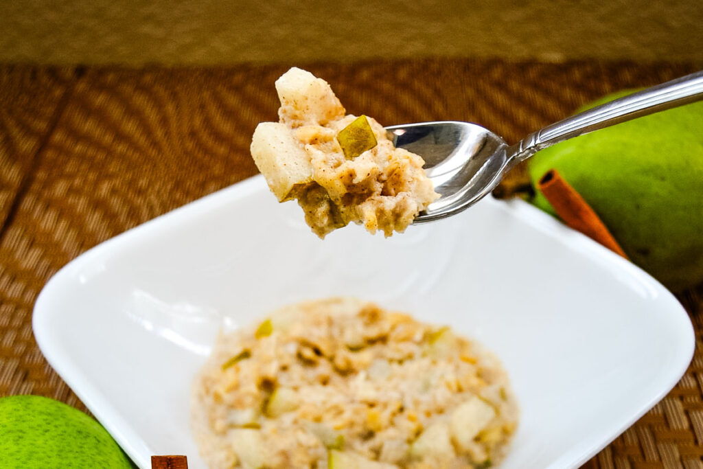Spiced Pear Overnight Oats on a spoon showy the chunky texture over a white bowl with the rest of the serving.
