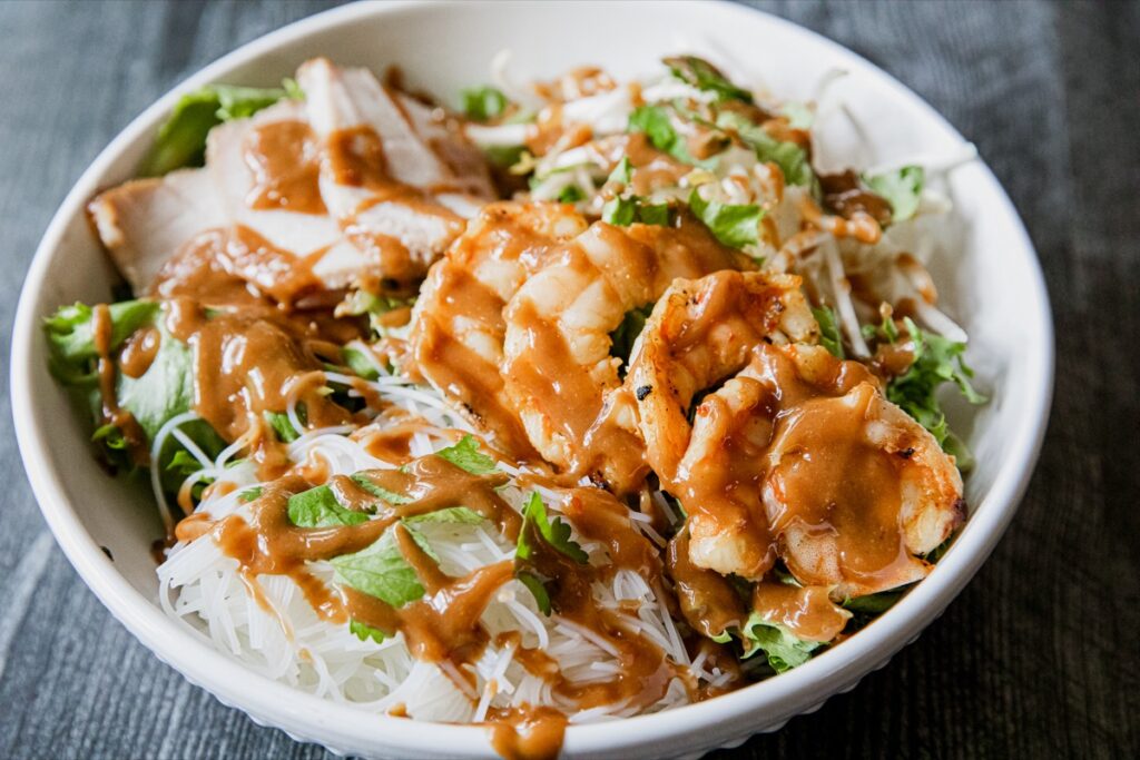 Spring roll bowl with rice noodles, fresh vegetables, and sauce arranged in a colorful bowl.