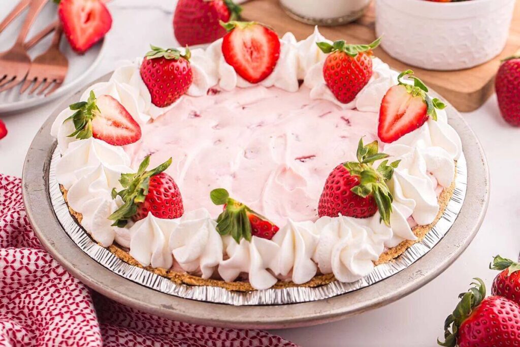 A delightful Strawberry Cool Whip Pie graces the table, adorned with lush whipped cream and fresh strawberries.