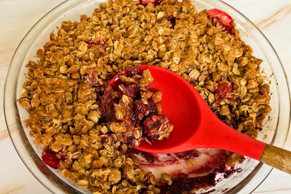 A baked strawberry berry crisp with oatmeal and blackberries in a clear dish with a portion removed.