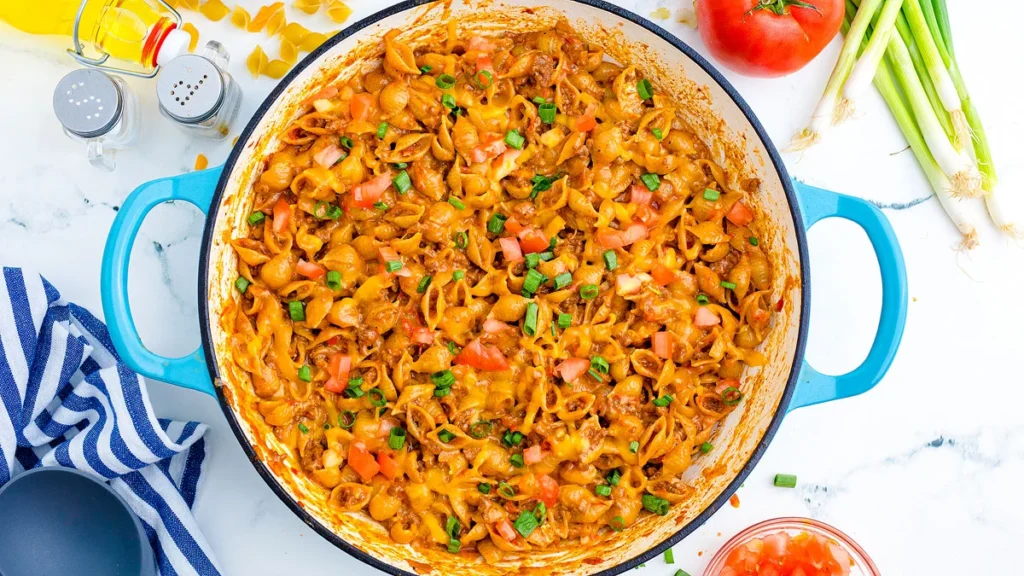 Taco macaroni and cheese served in a bowl, featuring seasoned ground beef, elbow pasta coated in melted cheese sauce, and topped with fresh herbs for garnish.