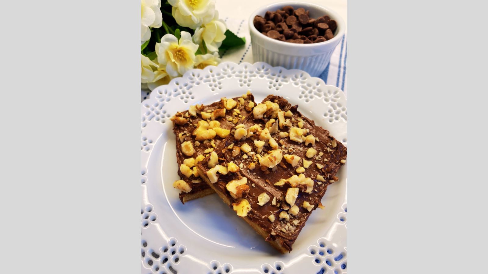 Two toffee cookies on white plate with bowl of chocolate chips in background.