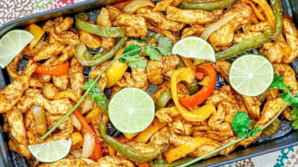 A tray of chicken fajitas with bell peppers, onions, lime slices, and cilantro garnish.