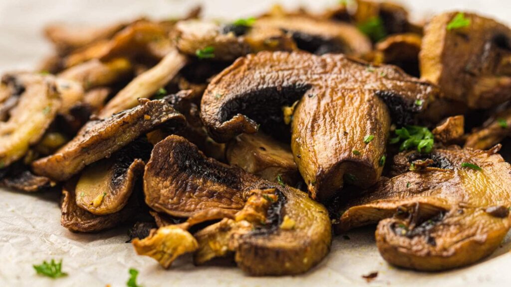 Close-up of sliced, cooked mushrooms garnished with small pieces of fresh herbs on a light-colored surface.