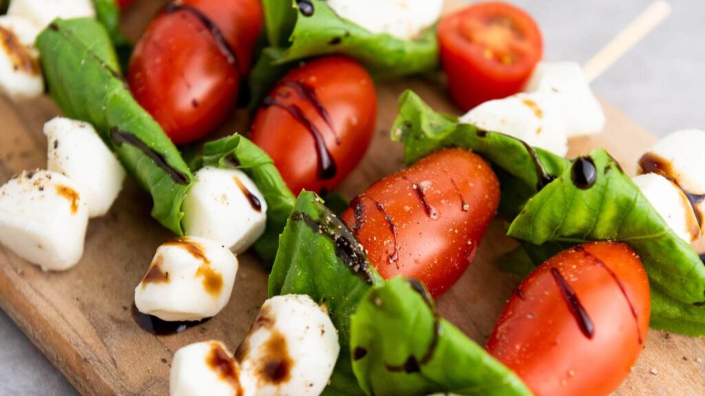 Caprese skewers drizzled with balsamic glaze on a wooden board.