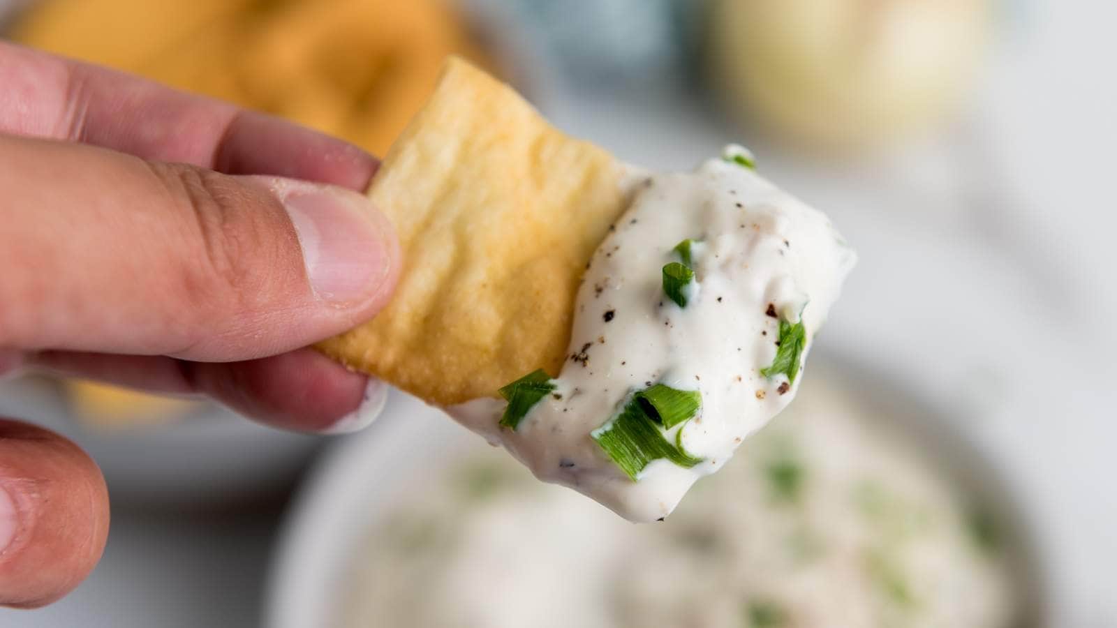 Close-up of a hand holding a cracker dipped in caramelized onion dip.