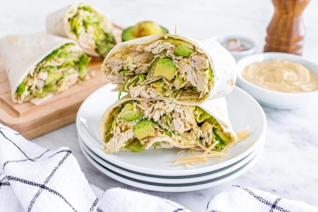 Close-up of chicken Caesar avocado wraps cut in half, served on stacked white plates.