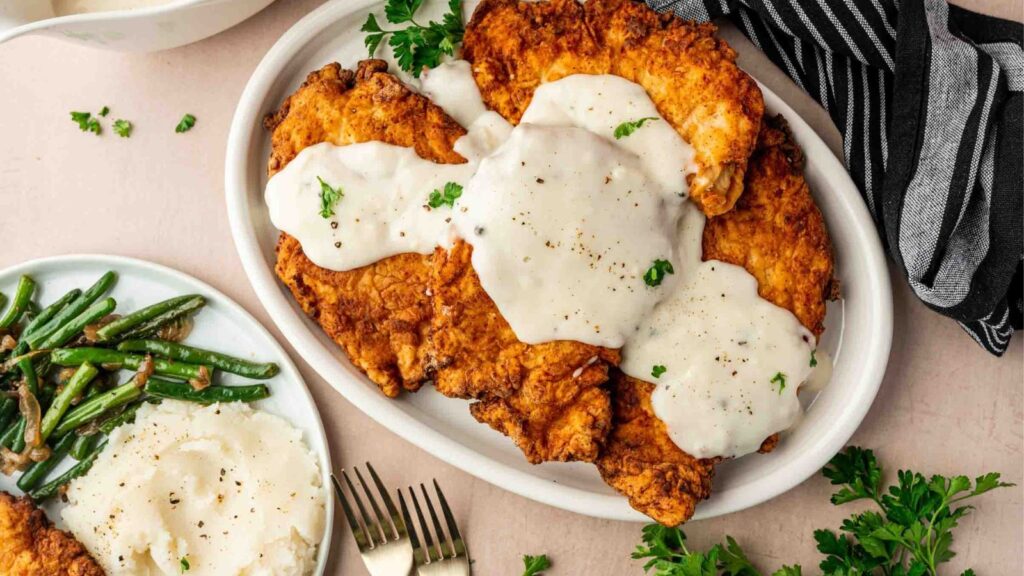 Crispy chicken-fried chicken covered in rich white gravy on a warm dinner plate.