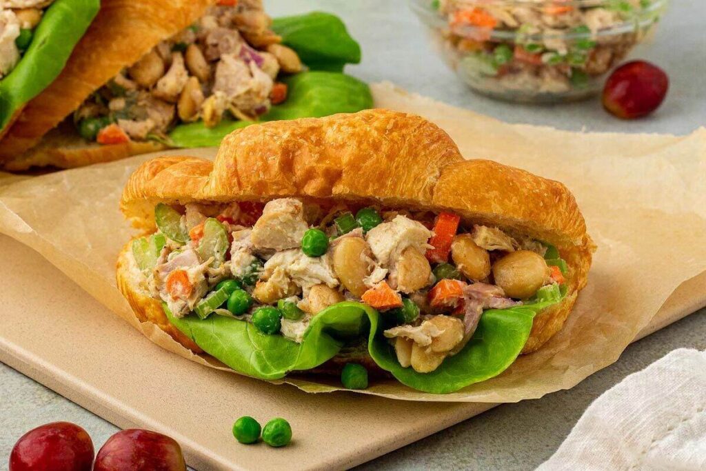 A chicken salad sandwich made with rotisserie chicken. Served with lettuce on a croissant, accompanied by grapes on the side.