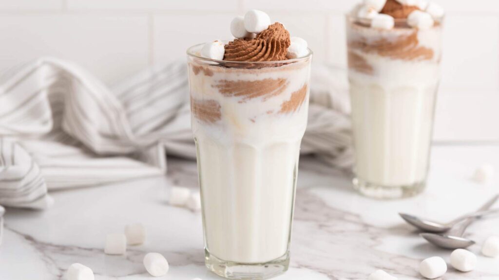 A creamy chocolate drink served in a tall glass. Another glass with a similar drink is partially visible in the background.