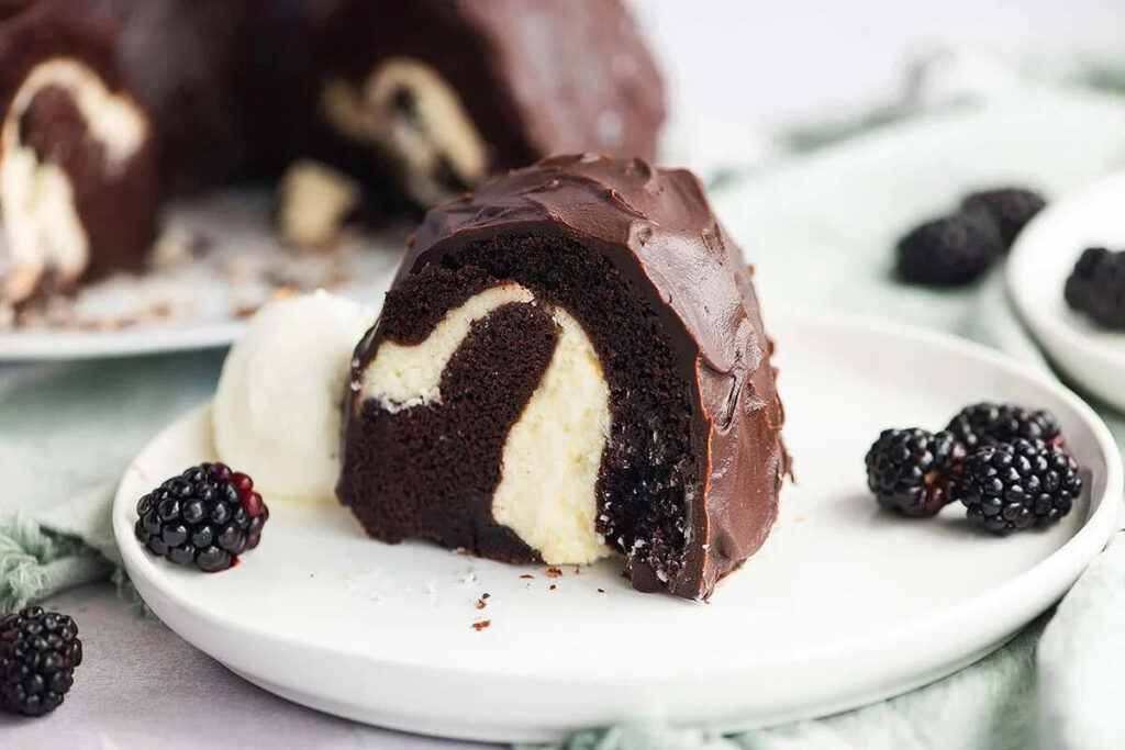 A slice of Chocolate Bundt Cake With Cream Cheese Filling, served with vanilla ice cream and blackberries, features a luscious cream cheese swirl for an irresistible treat.