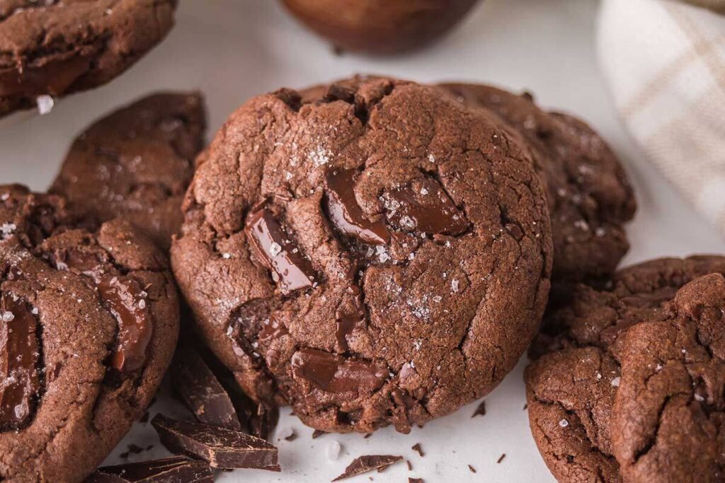 Close-up of chocolate fudge cookies adorned with chunks of rich chocolate and a sprinkle of sea salt, elegantly arranged on a light surface.