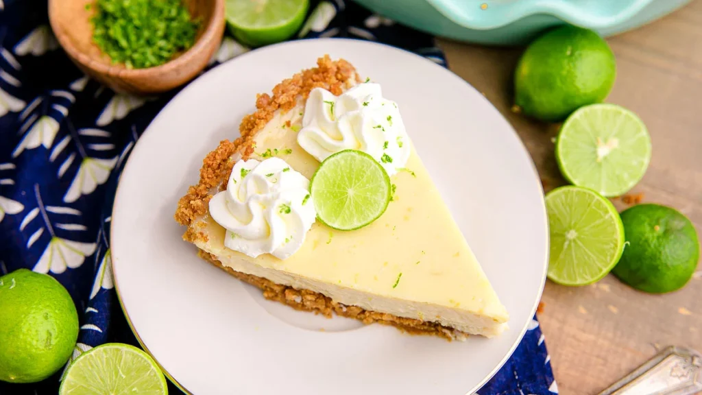 Slice of key lime pie with whipped cream and a lime slice on top on a plate.